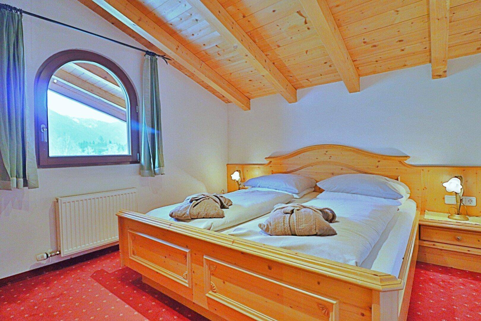 Helles Schlafzimmer mit Holzbett, rotem Teppich und einem charmanten Rundbogenfenster.