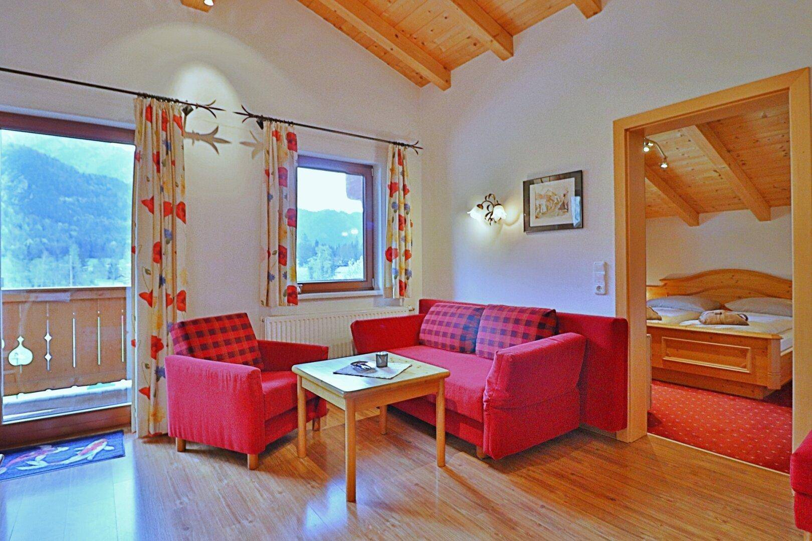 Wohnbereich mit rotem Sofa, Holzboden und Zugang zu einem Schlafzimmer.