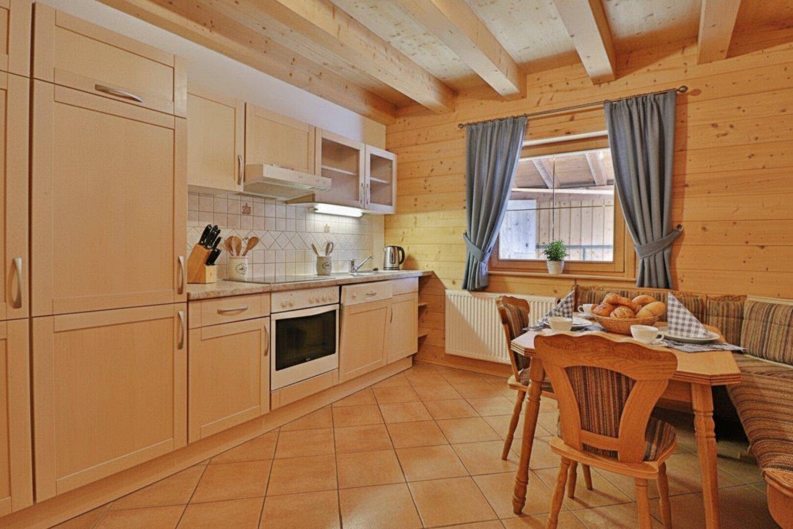 Funktionale Küche mit hellen Holzschränken, Fliesenboden und einem kleinen Essbereich am Fenster.