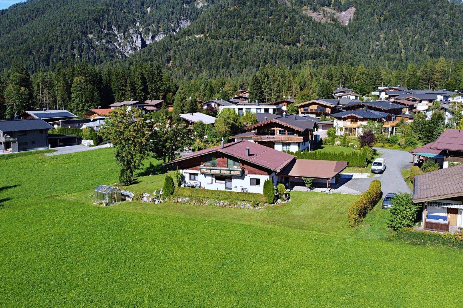 Luftaufnahme des Hauses mit Garten und der umliegenden Wohnsiedlung in alpiner Landschaft.