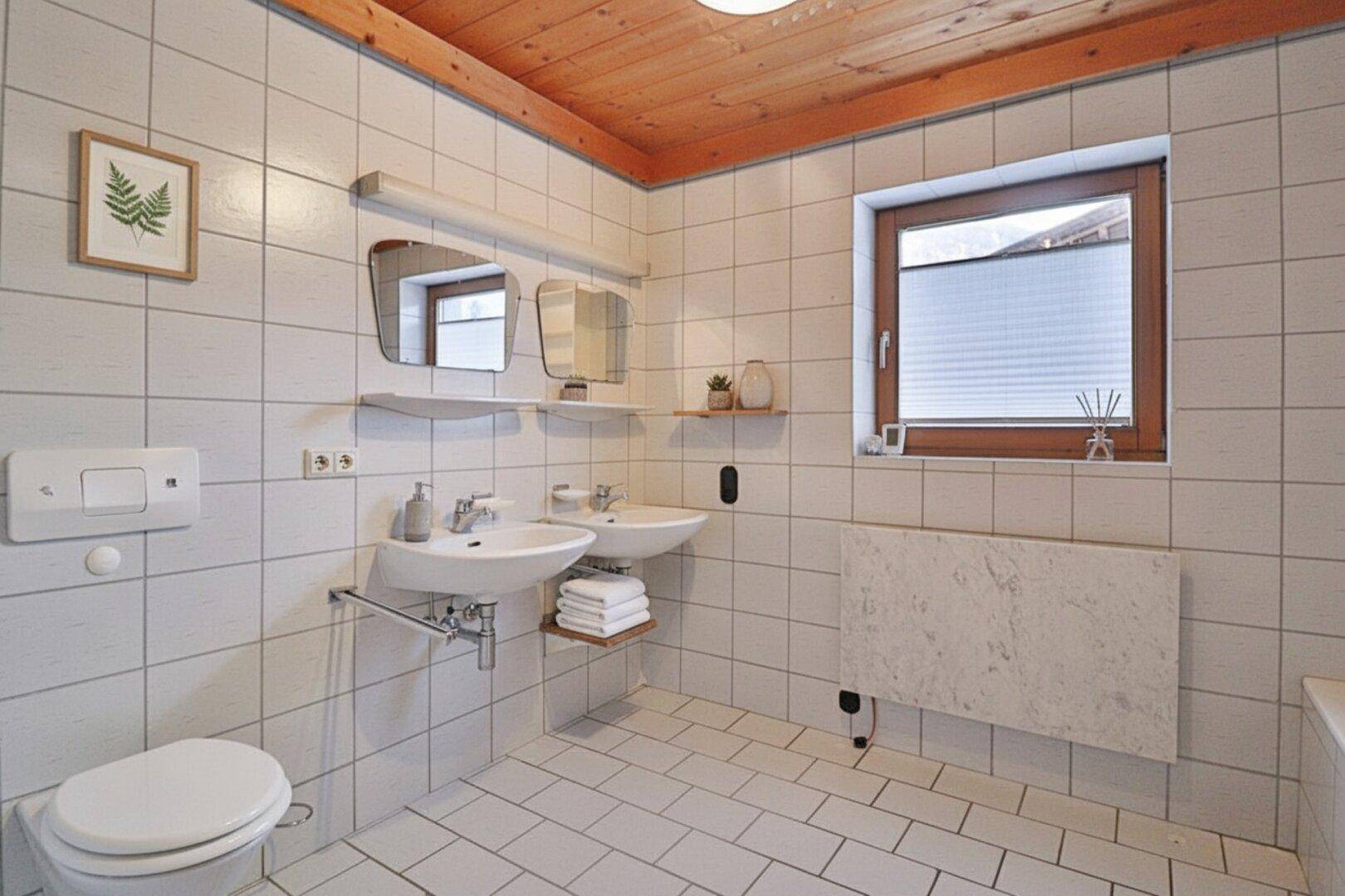 Funktionales Badezimmer mit Doppelwaschbecken, Fenster und Holzdecke.