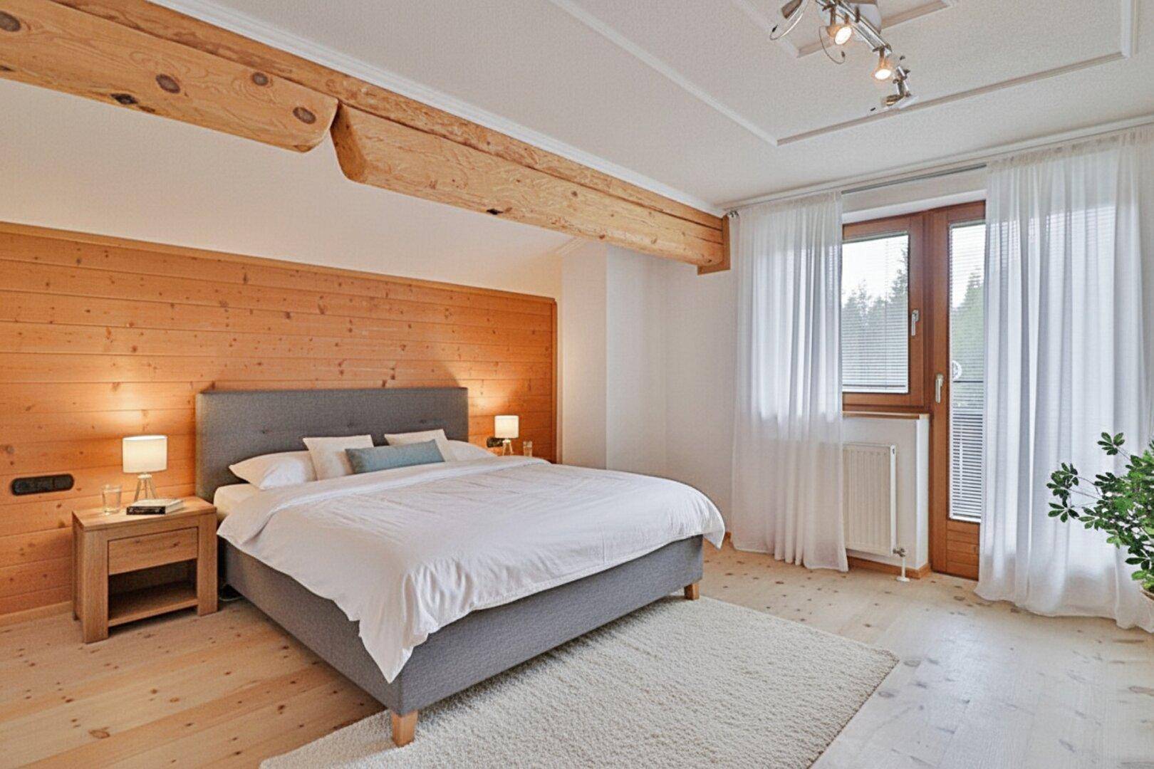 Geräumiges Schlafzimmer mit Holzwand, sichtbaren Balken und Zugang zum Balkon.