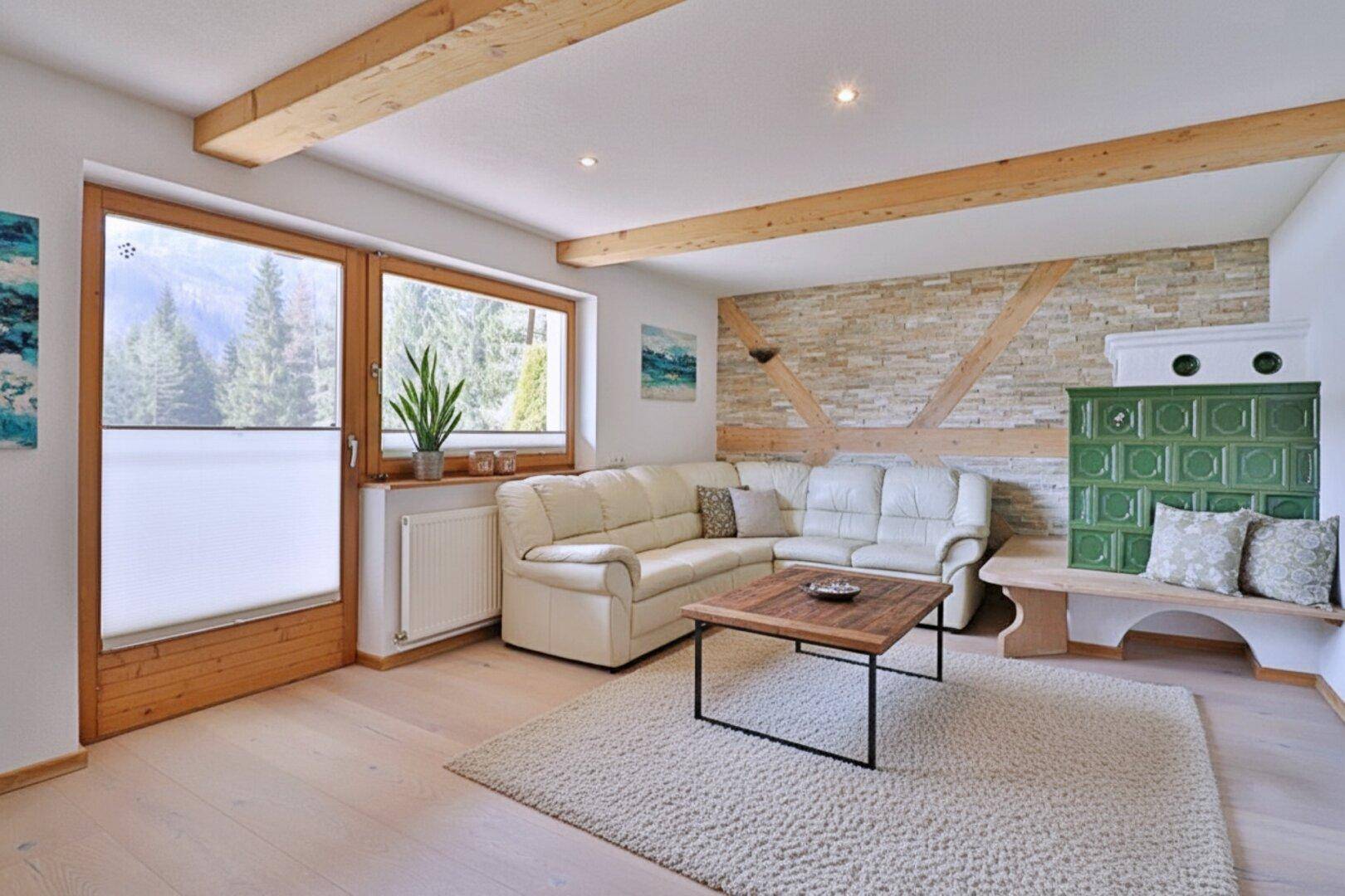 Gemütliches Wohnzimmer mit hellem Holzboden, sichtbaren Holzbalken und traditionellem Kachelofen.