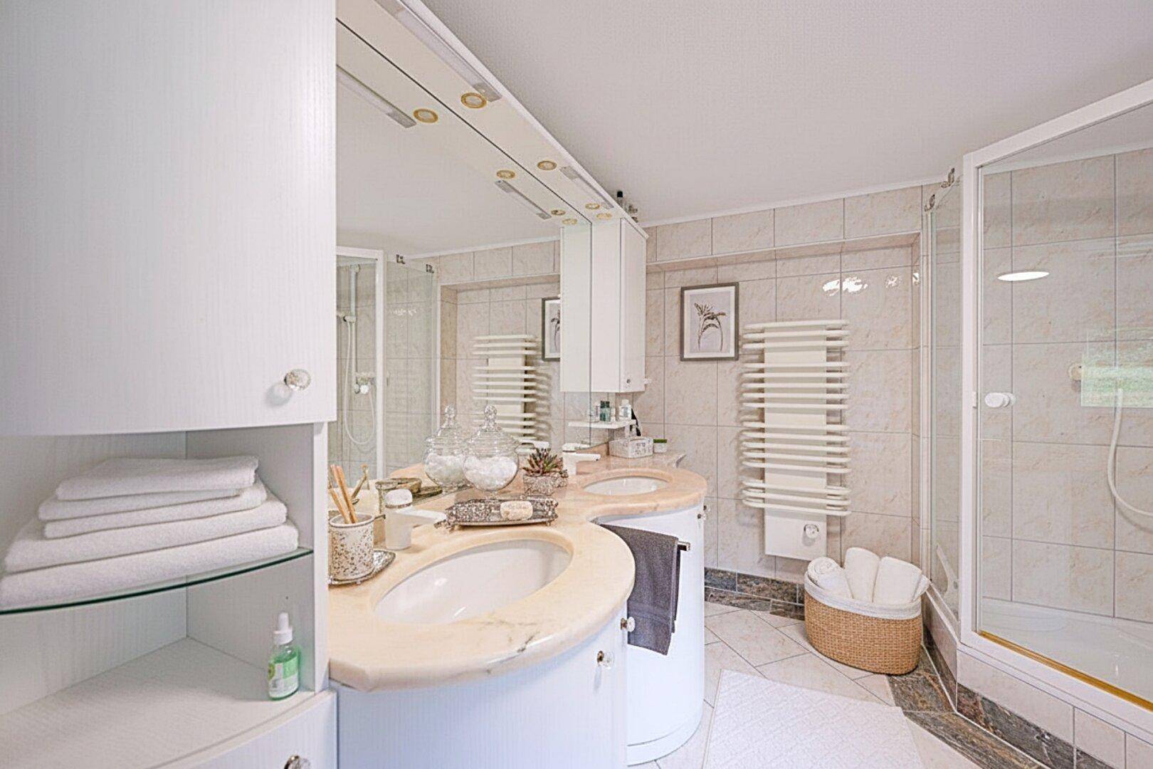 Helles Badezimmer mit Doppelwaschbecken, Dusche und beheiztem Handtuchhalter.