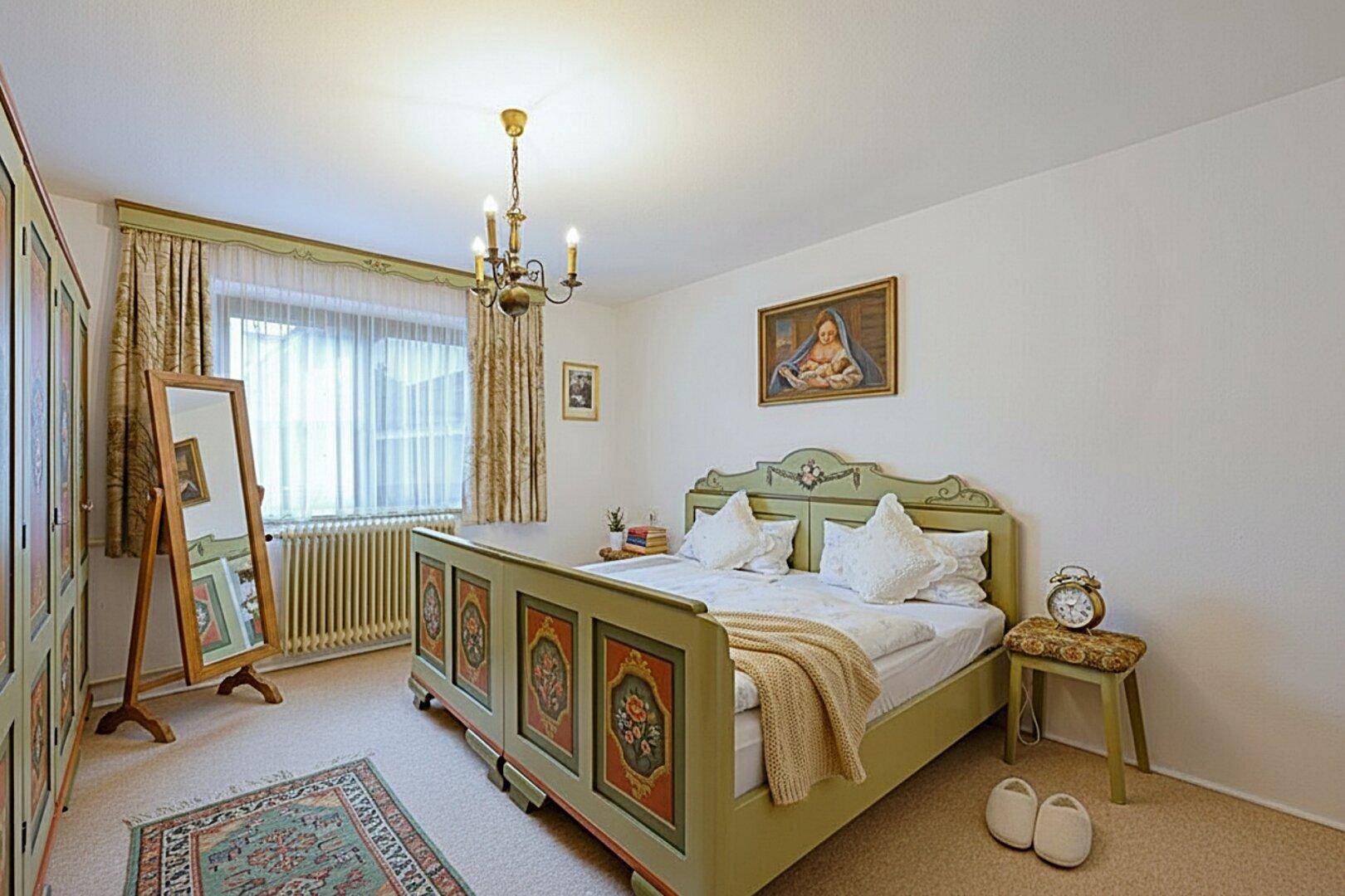 Schlafzimmer mit traditionellem, handbemaltem Bett, Teppichboden und großem Spiegel.