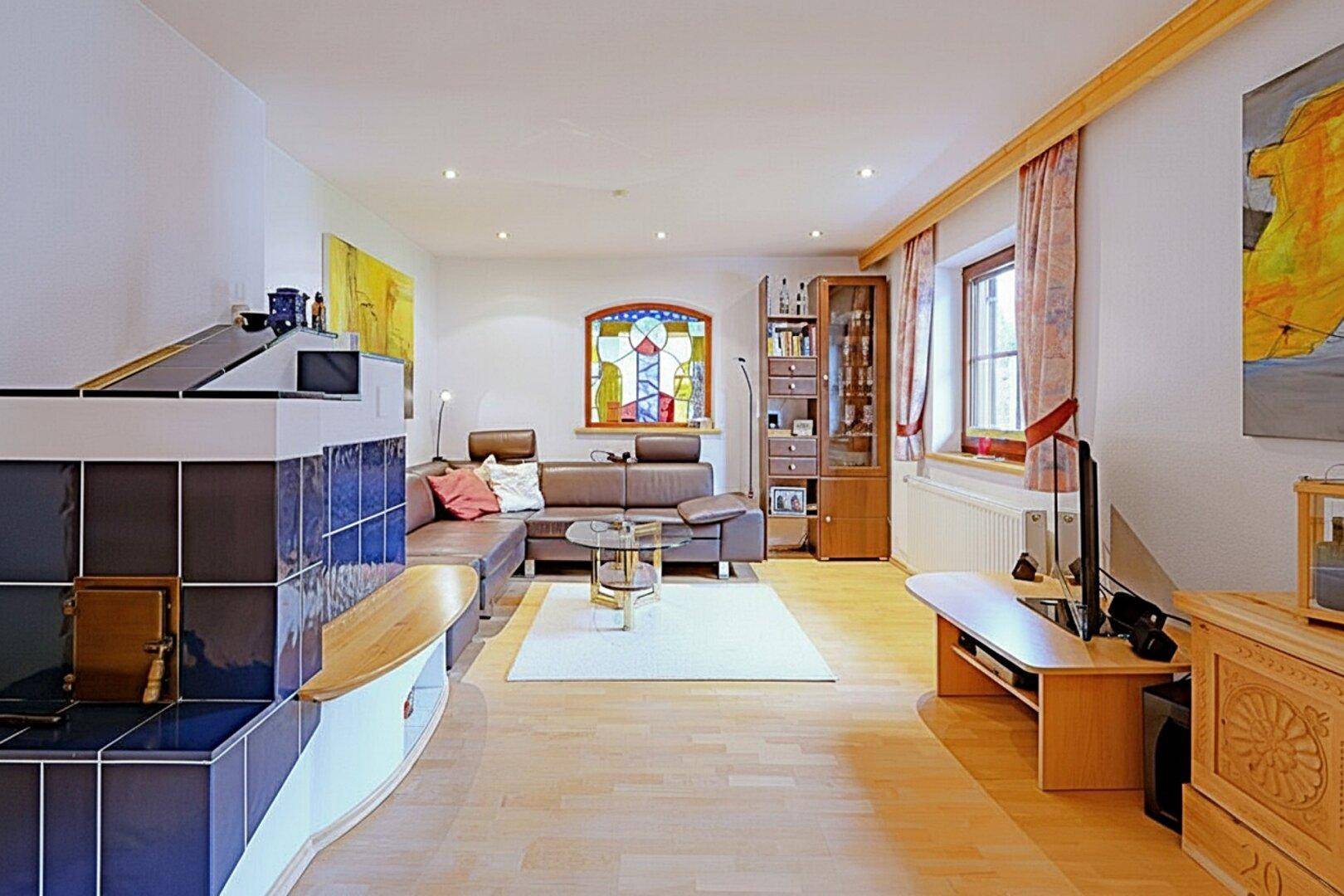 Helles Wohnzimmer mit Kachelofen, bequemer Ledercouch und farbigem Glasfenster.