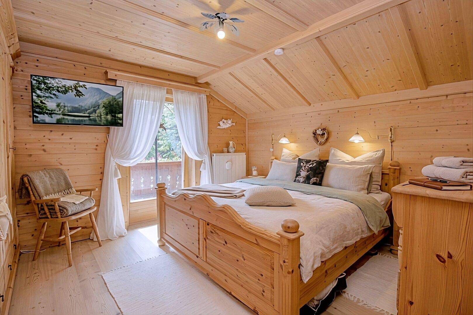 Helles Schlafzimmer mit Holztäfelung, Dachschräge und Zugang zu einem kleinen Balkon.