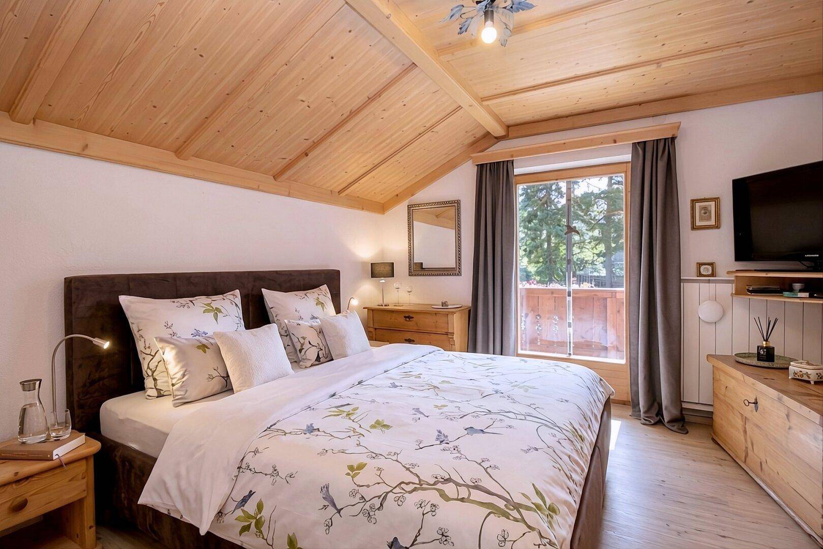 Gemütliches Schlafzimmer mit Holzbalkendecke, großem Bett und Blick ins Grüne.