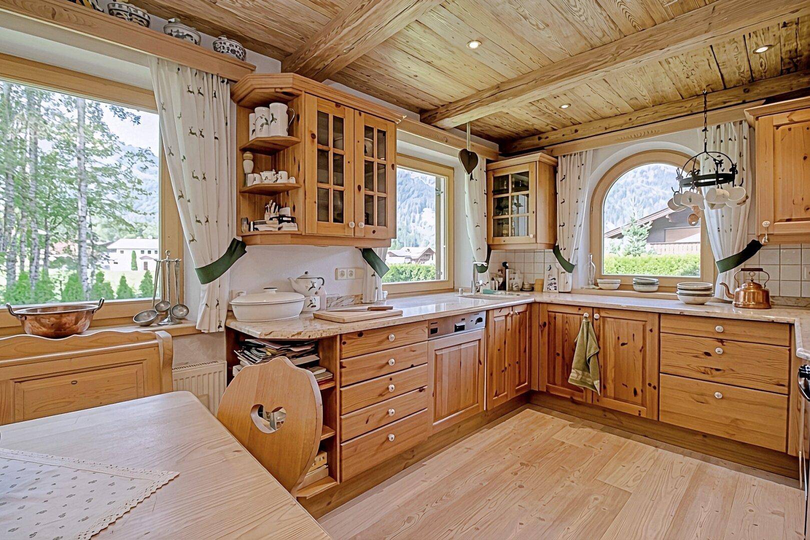 Rustikale Holzküche mit vielen Fenstern, hellen Arbeitsplatten und Blick auf die Berge.