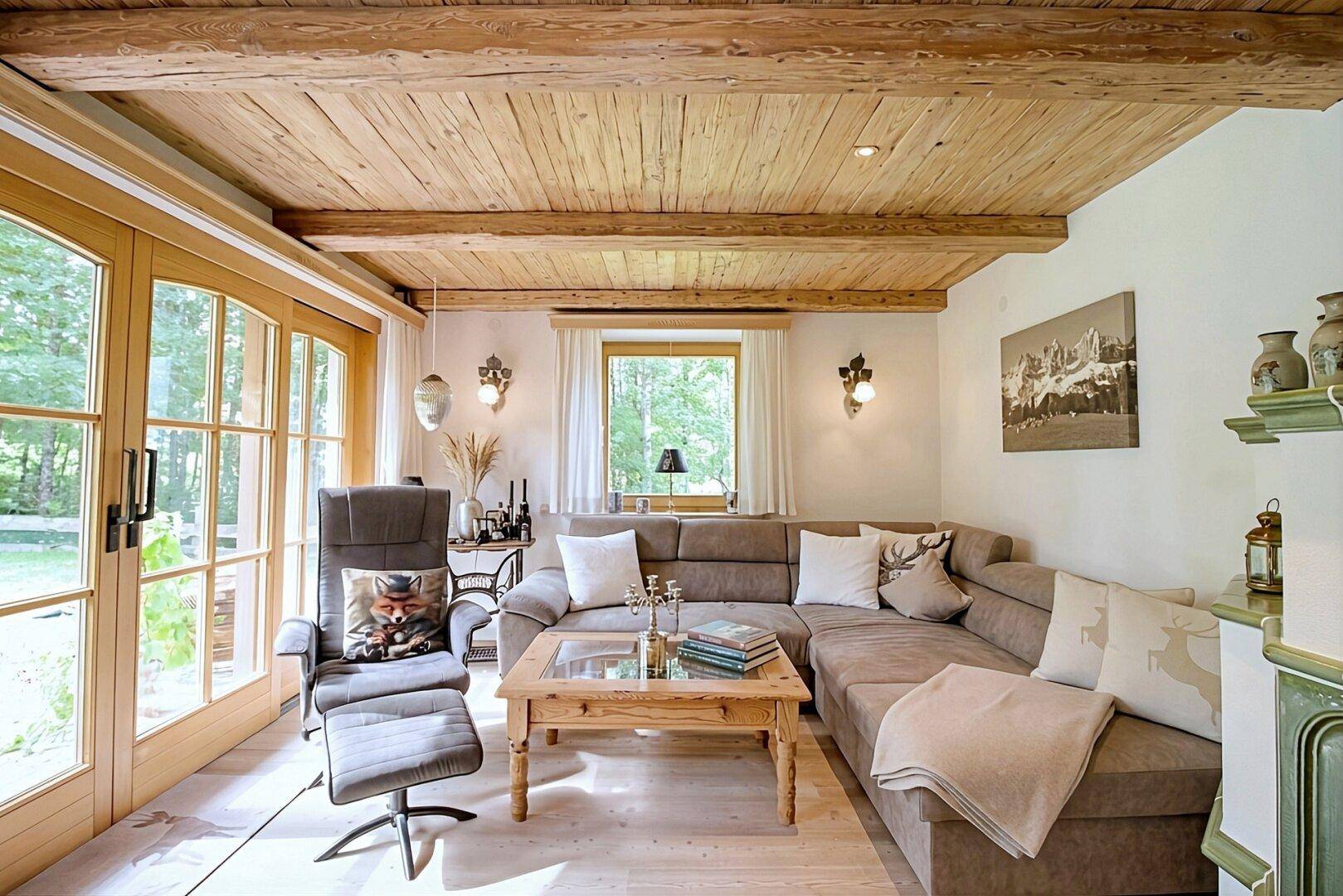 Gemütliches Wohnzimmer im alpinen Stil mit Holzbalkendecke und großen Fenstern zum Garten.