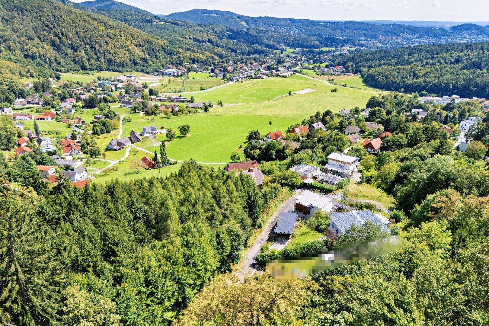 Panoramablick über ein Tal mit einer Siedlung, umgeben von grünen Hügeln und Wäldern.