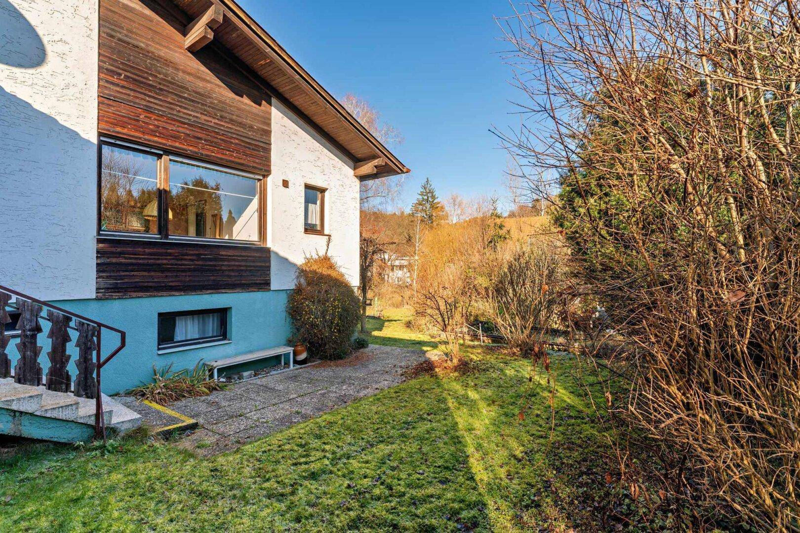 Hausfassade mit Außentreppe und angrenzendem Gartenbereich mit Rasen und Sträuchern.