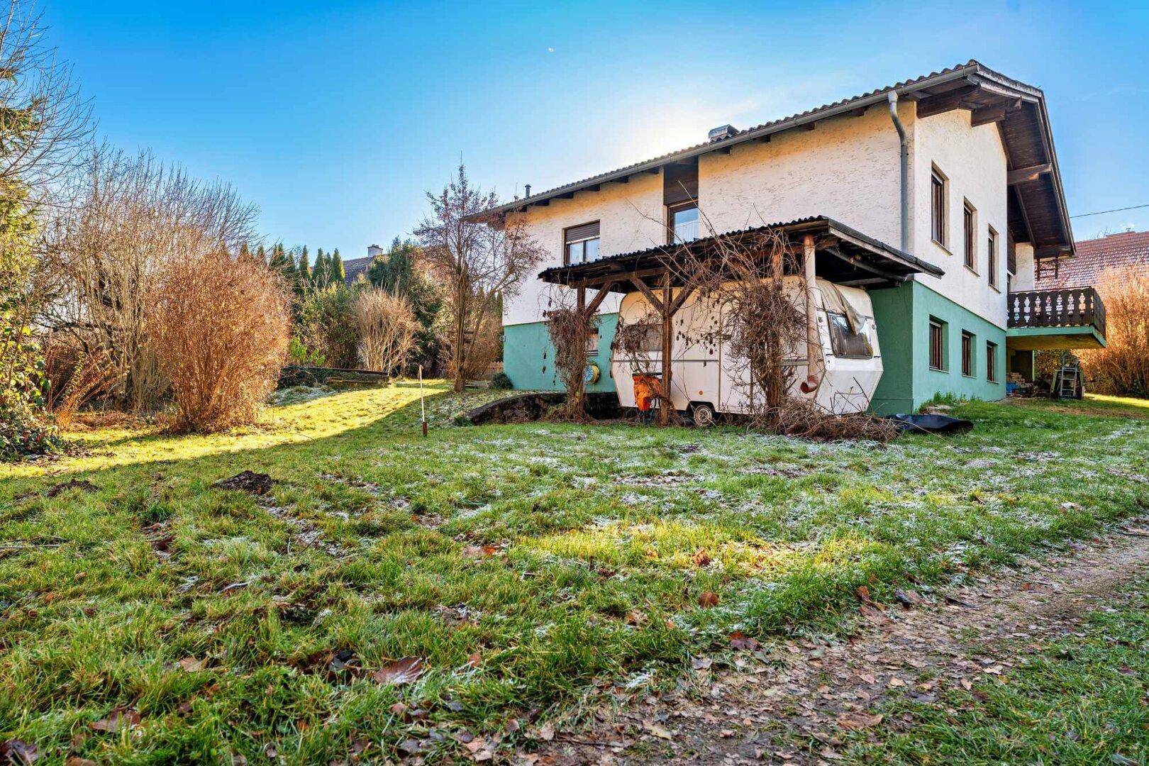 Rückseite des Hauses mit großem Garten, Rasenfläche und einem überdachten Bereich.