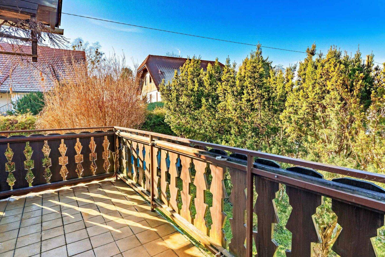 Traditioneller Holzbalkon mit Fliesenboden und Blick auf die umliegende grüne Landschaft.