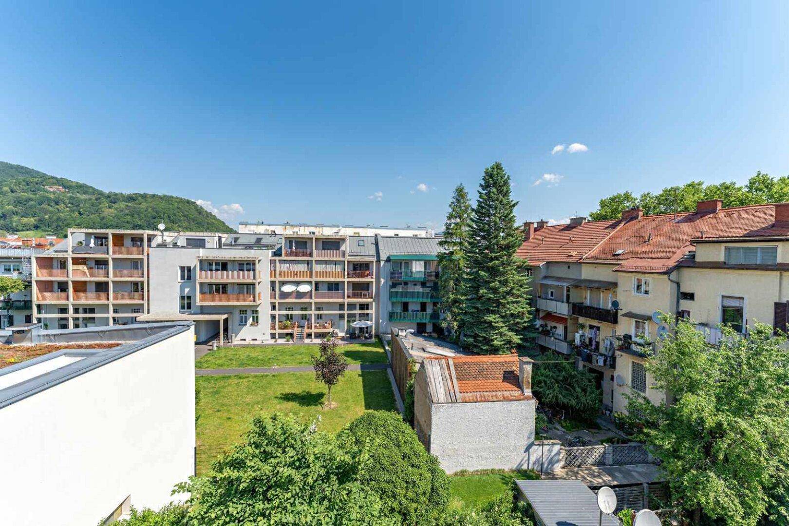 Blick über eine Wohnsiedlung mit Grünflächen und Bergen im Hintergrund.