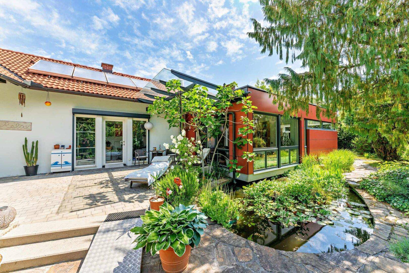 Weitläufige Terrasse mit Zugang zum Garten und Teich, unter einem sonnigen Himmel.