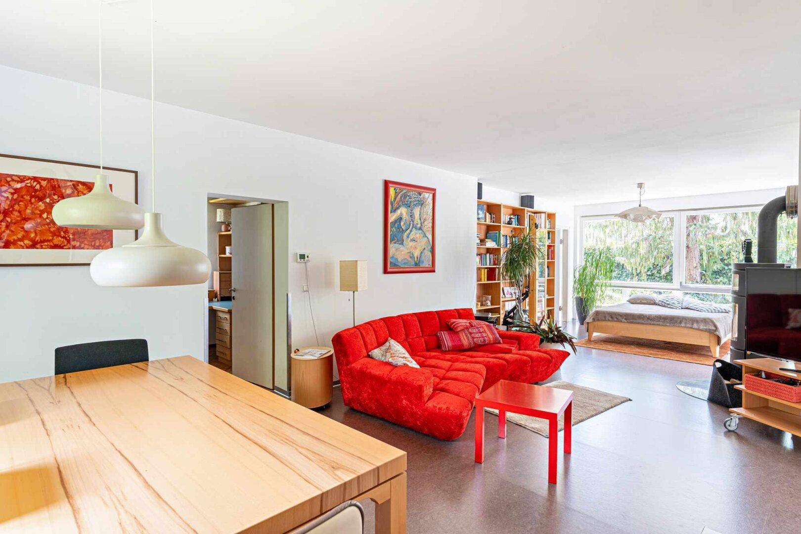 Geräumiger offener Wohnbereich mit rotem Sofa, Bücherregalen und gemütlichem Holzofen.
