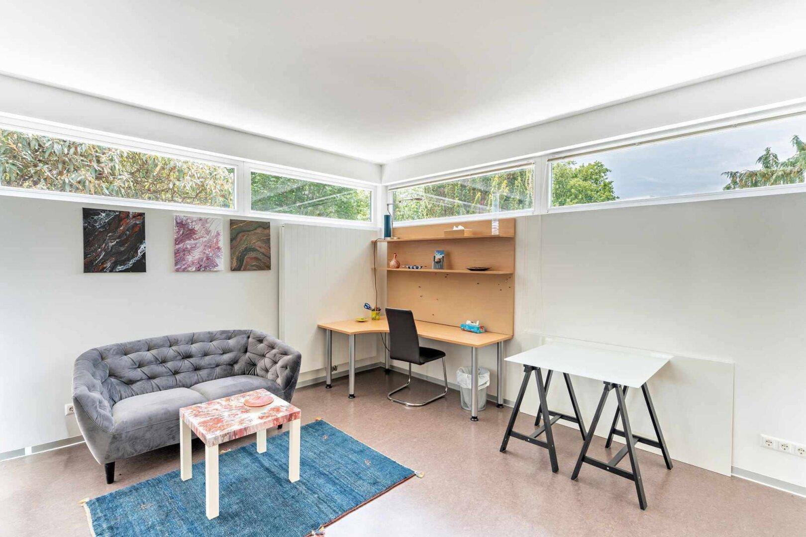 Helles Arbeitszimmer mit Schreibtisch, bequemer Couch und hohen Fenstern für viel Tageslicht.