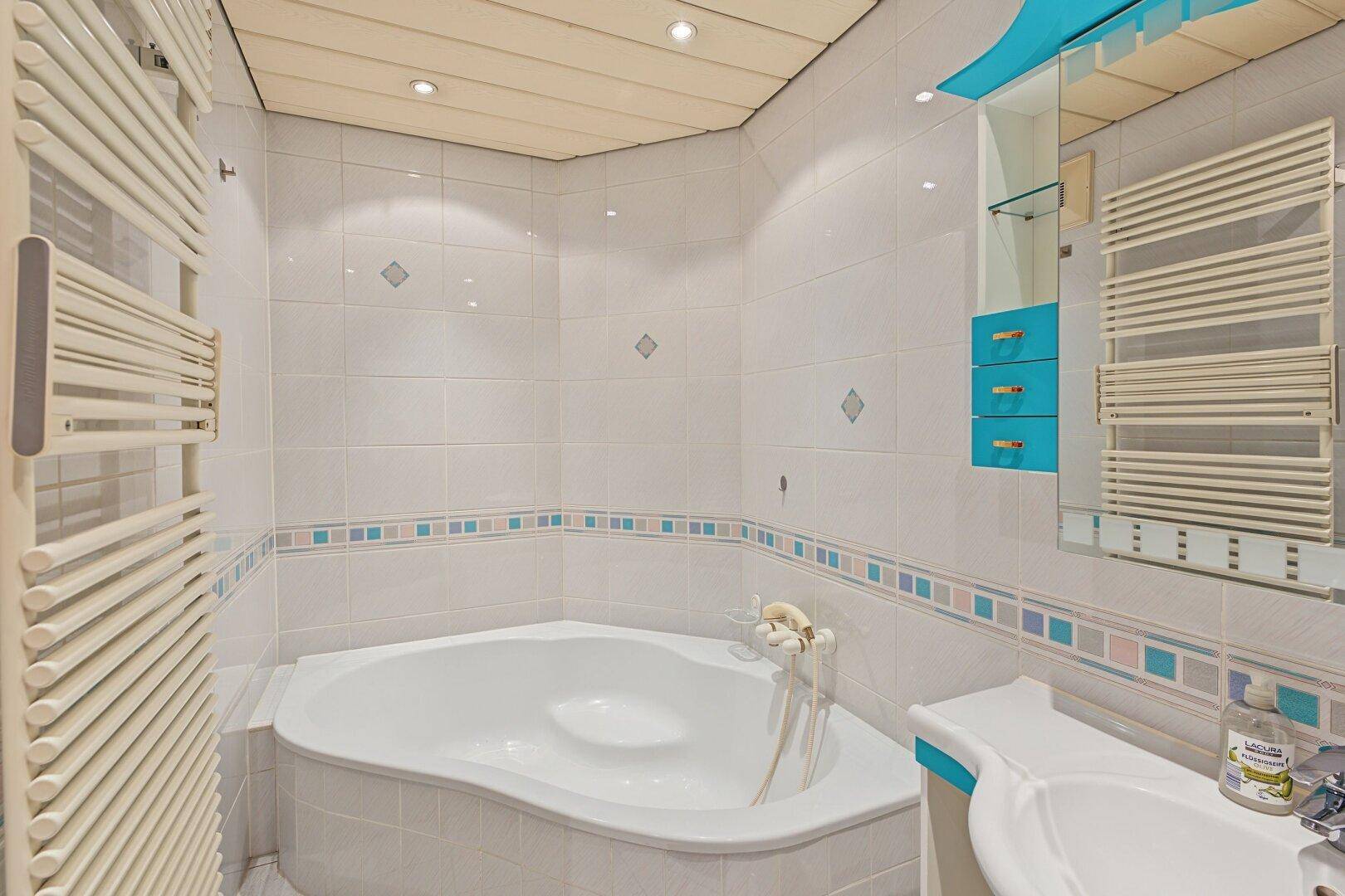 Badezimmer mit Eckbadewanne, Fliesenwänden und beheiztem Handtuchhalter.