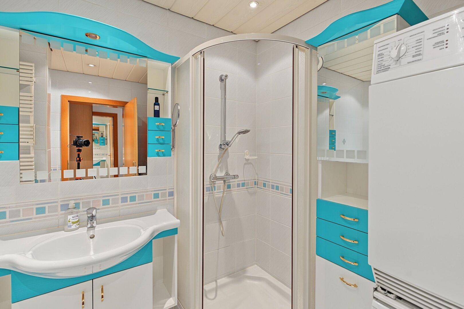 Badezimmer mit Duschkabine, Waschbecken, Spiegel und blauen Schränken.