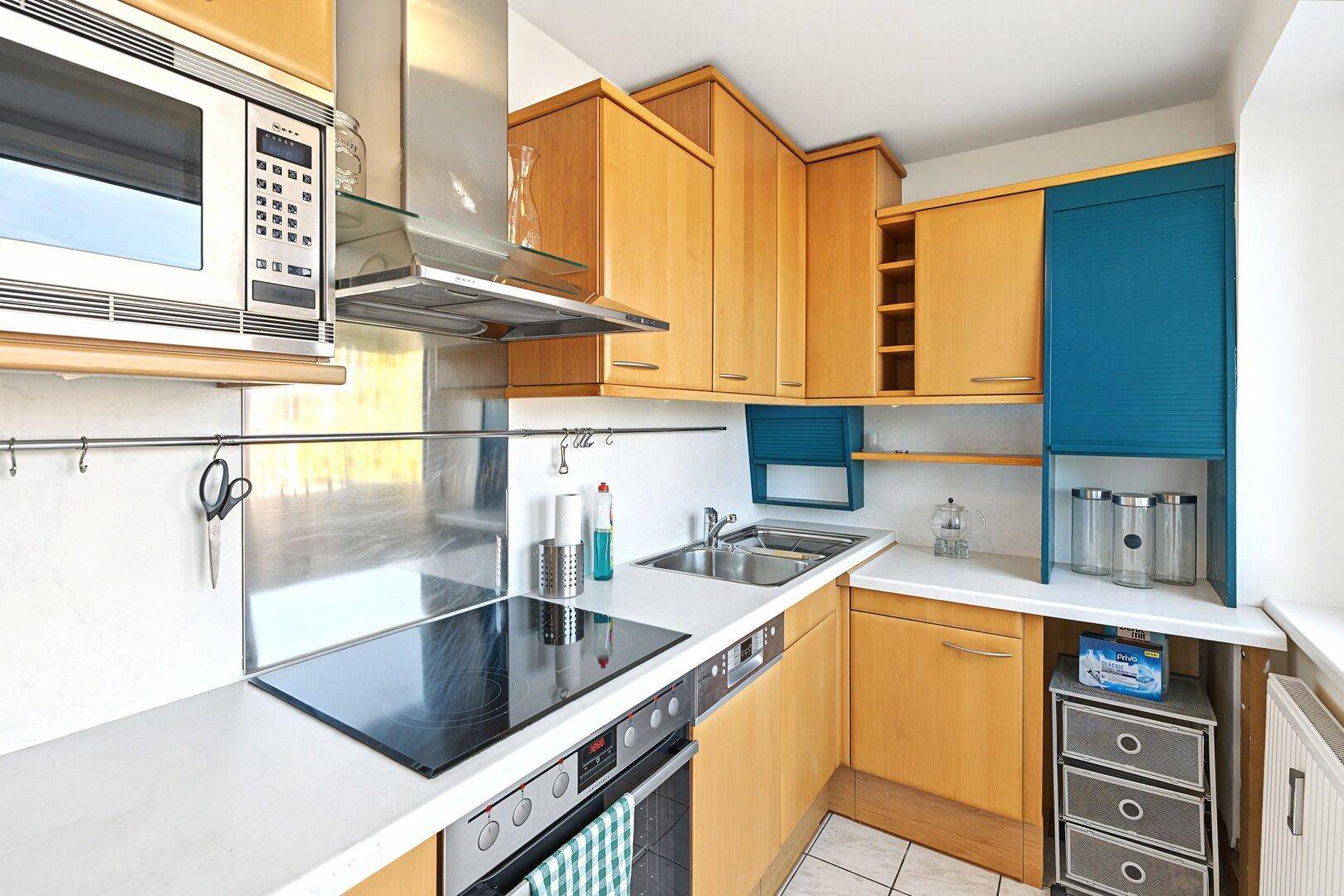 Funktionale Küche mit Holzschränken, modernen Geräten und blauen Akzenten.