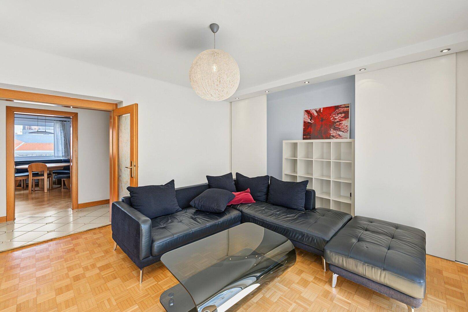 Gemütliches Wohnzimmer mit dunklem Sofa, Parkettboden und Blick in den Essbereich.