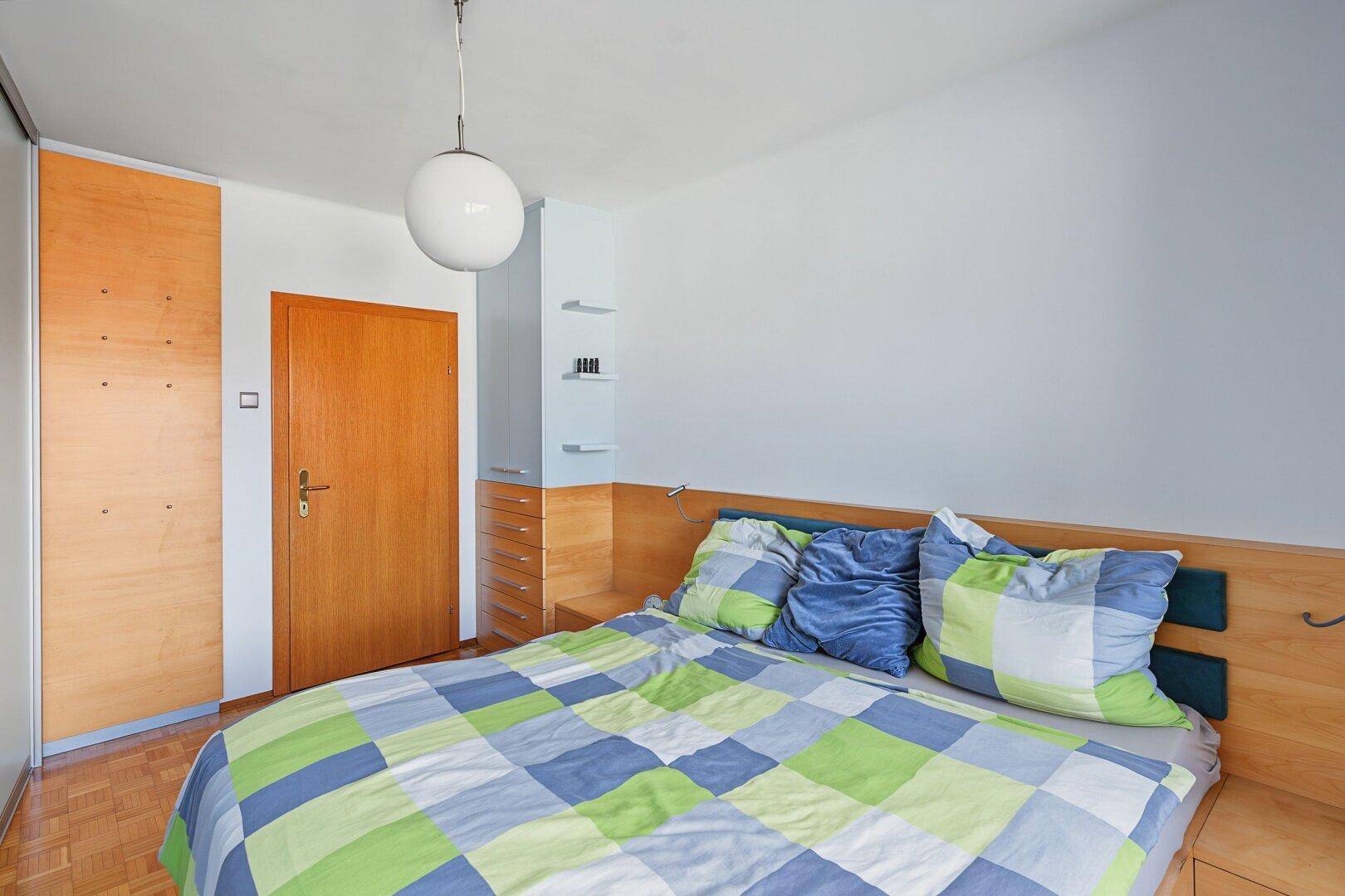 Schlafzimmer mit Holzelementen, farbenfroher Bettwäsche und integriertem Kleiderschrank.