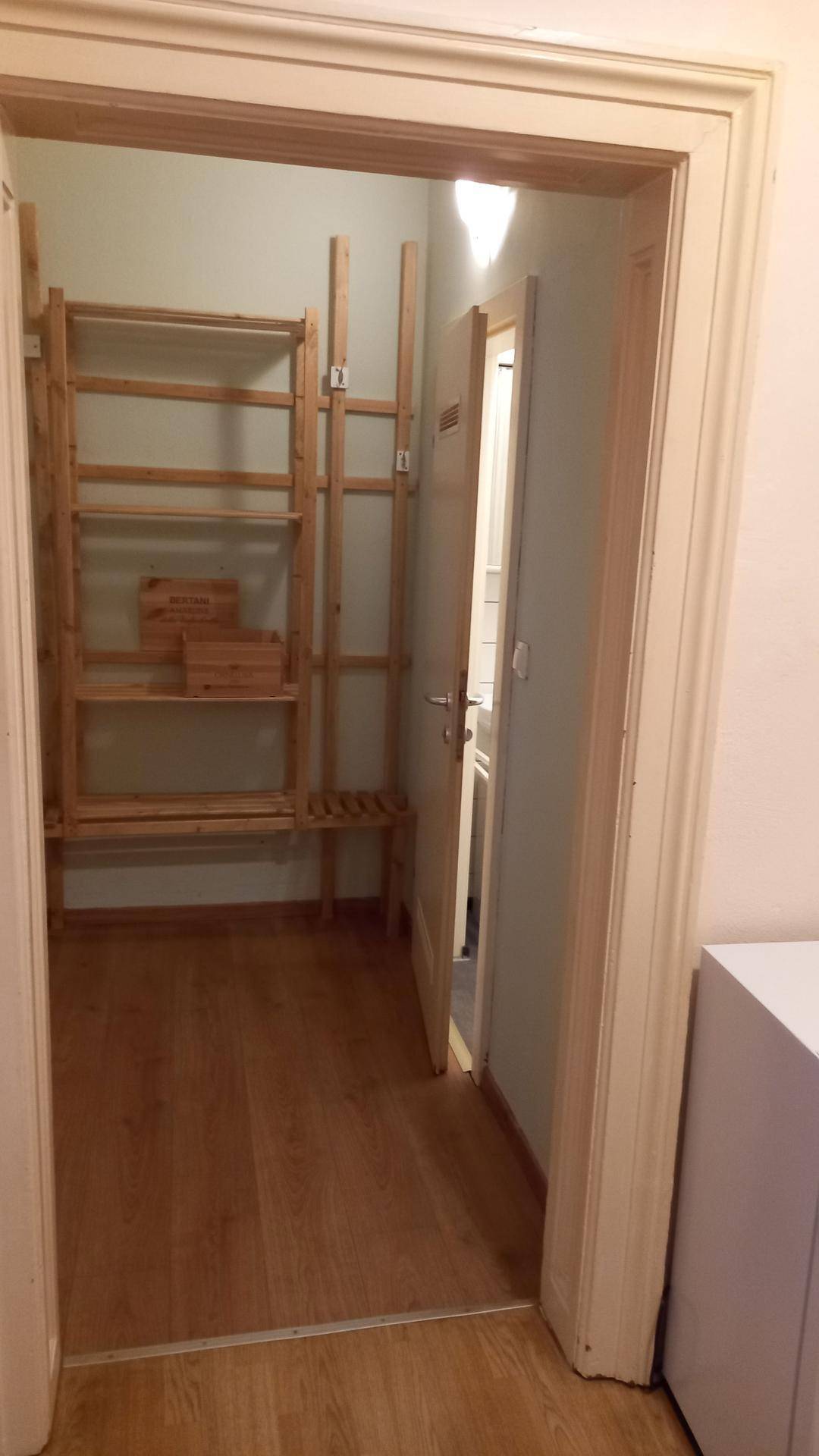 Abstellraum mit einfachen Holzregalen, ideal für zusätzlichen Stauraum, mit Zugang zu einem weiteren Raum.
