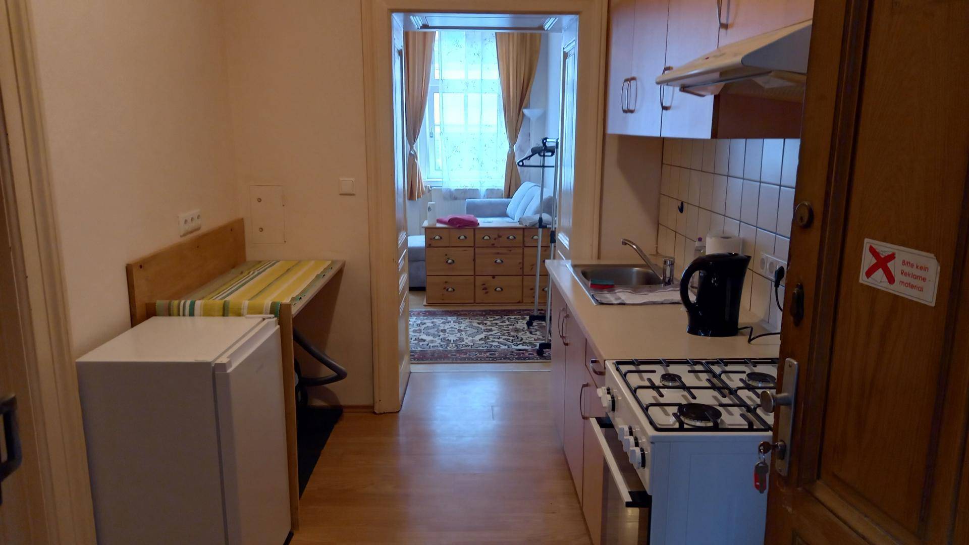 Kleine Küche mit Gasherd, Spüle und Kühlschrank, die zum Wohnbereich hin offen ist.