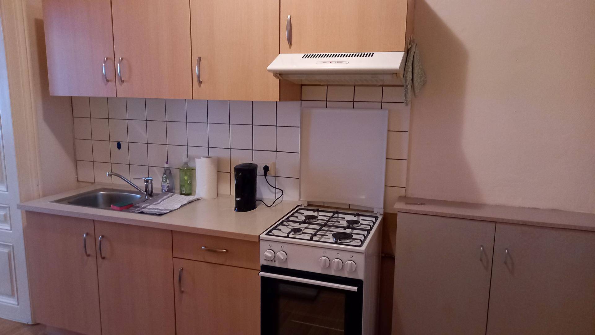Detailansicht der Küche mit Gasherd, Spülbecken und hellen Holzschränken über gefliestem Bereich.