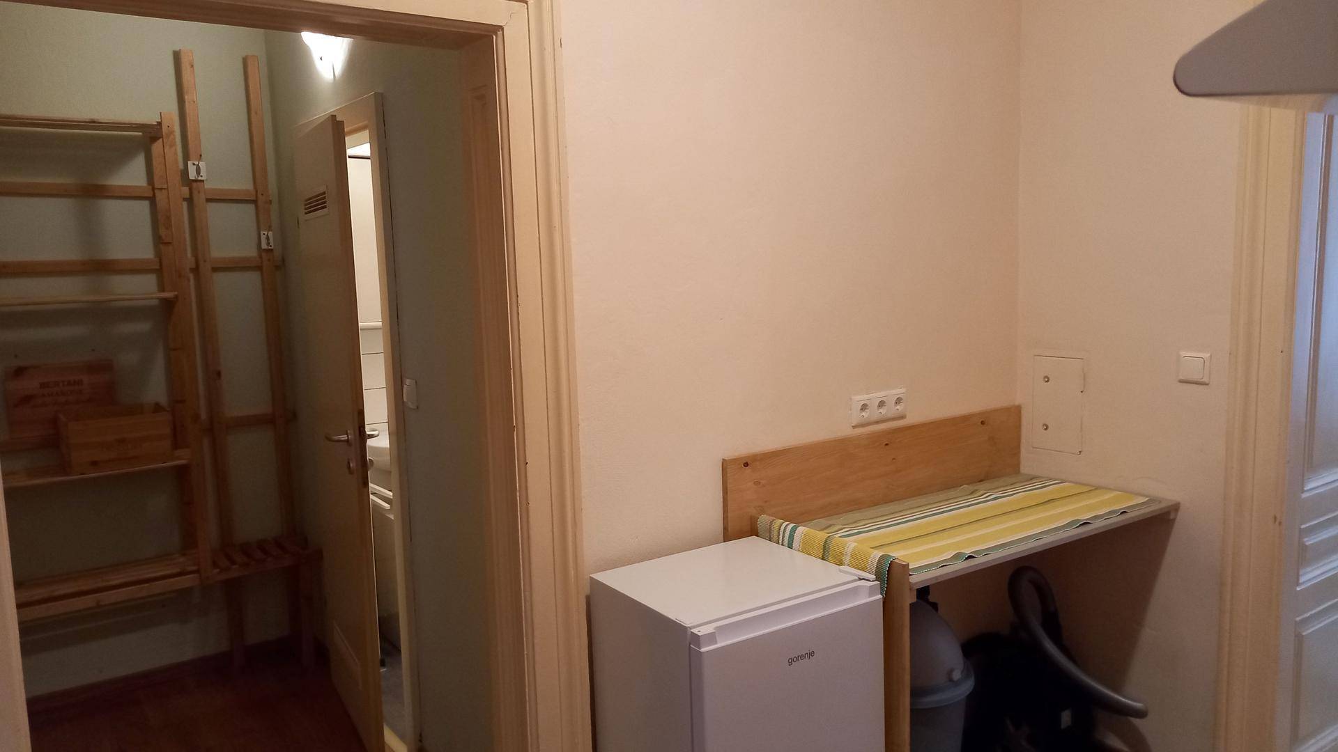 Praktischer Abstellraum mit Holzregalen, kleinem Kühlschrank und einem Klapptisch.