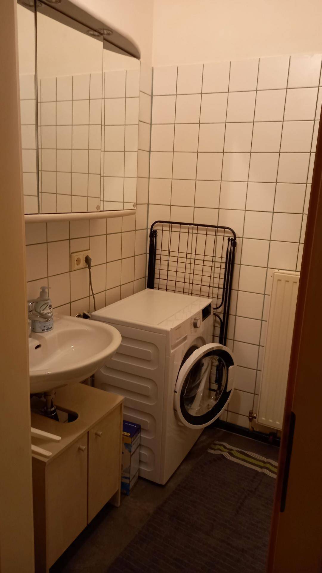 Badezimmer mit Waschbecken, Spiegelschrank und Waschmaschine, ausgestattet mit weißen Fliesen.