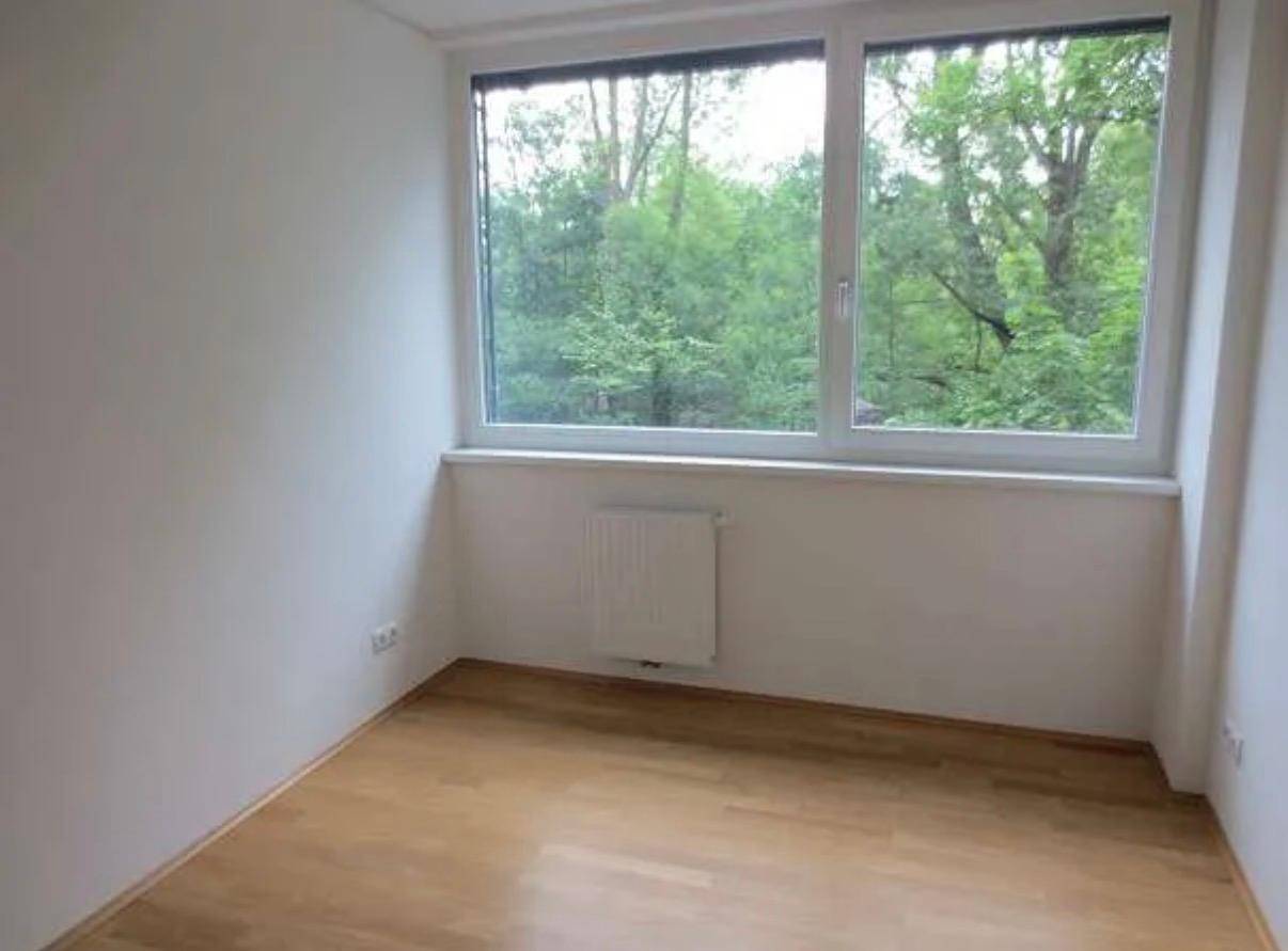 Leeres Zimmer mit Parkettboden und Fenster mit Blick ins Grüne.