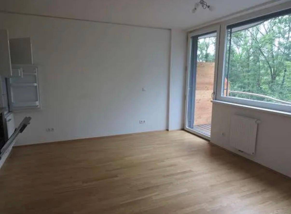 Heller Wohnbereich mit Parkettboden, großen Fenstern und Zugang zum Balkon mit Grünblick.