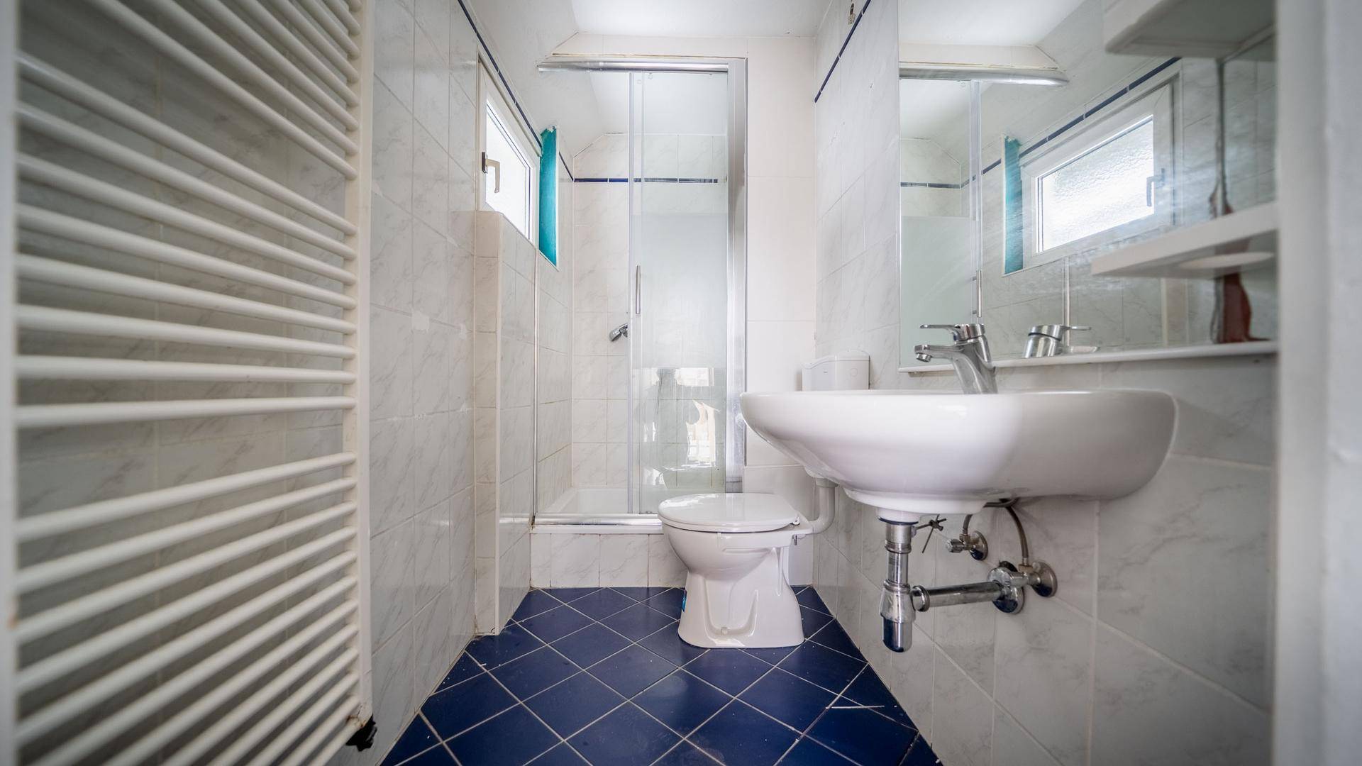Funktionales Badezimmer mit blauen Fliesen, Duschkabine, WC, Waschbecken und beheiztem Handtuchhalter.