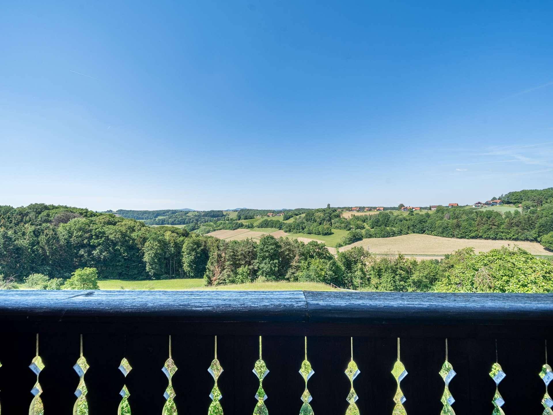 Malerischer Ausblick vom Balkon über sanfte Hügel und weite Felder unter blauem Himmel.