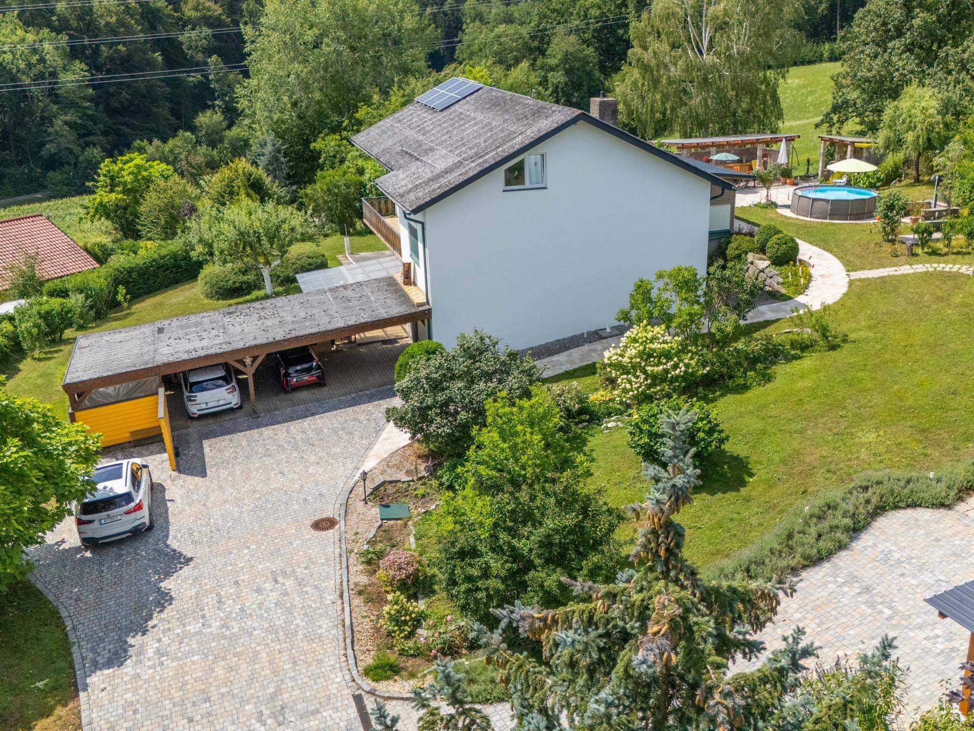 Luftaufnahme des Hauses mit Carport, Garten und oberirdischem Pool in grüner Umgebung.