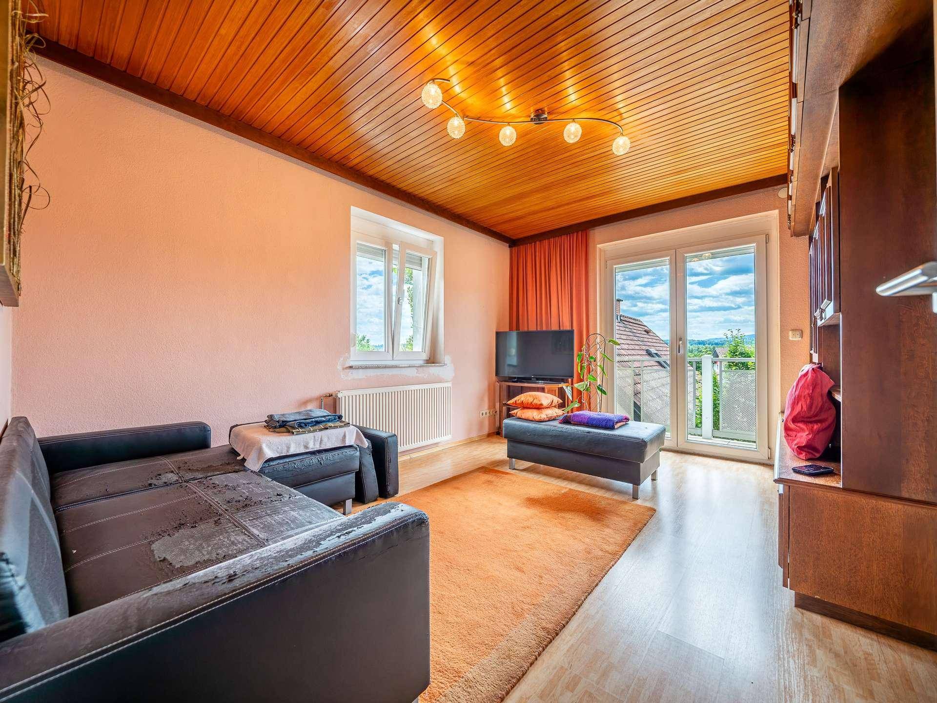 Wohnzimmer mit Holzbalkendecke, Sofa und Zugang zum Balkon mit Weitblick.