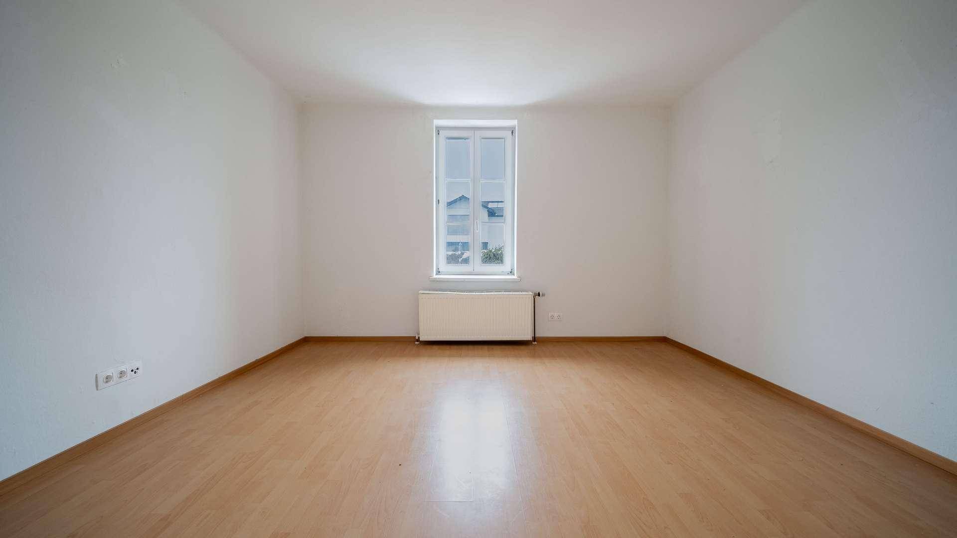 Geräumiges Schlafzimmer mit Laminatboden, weiß gestrichenen Wänden und einem zentralen Fenster.