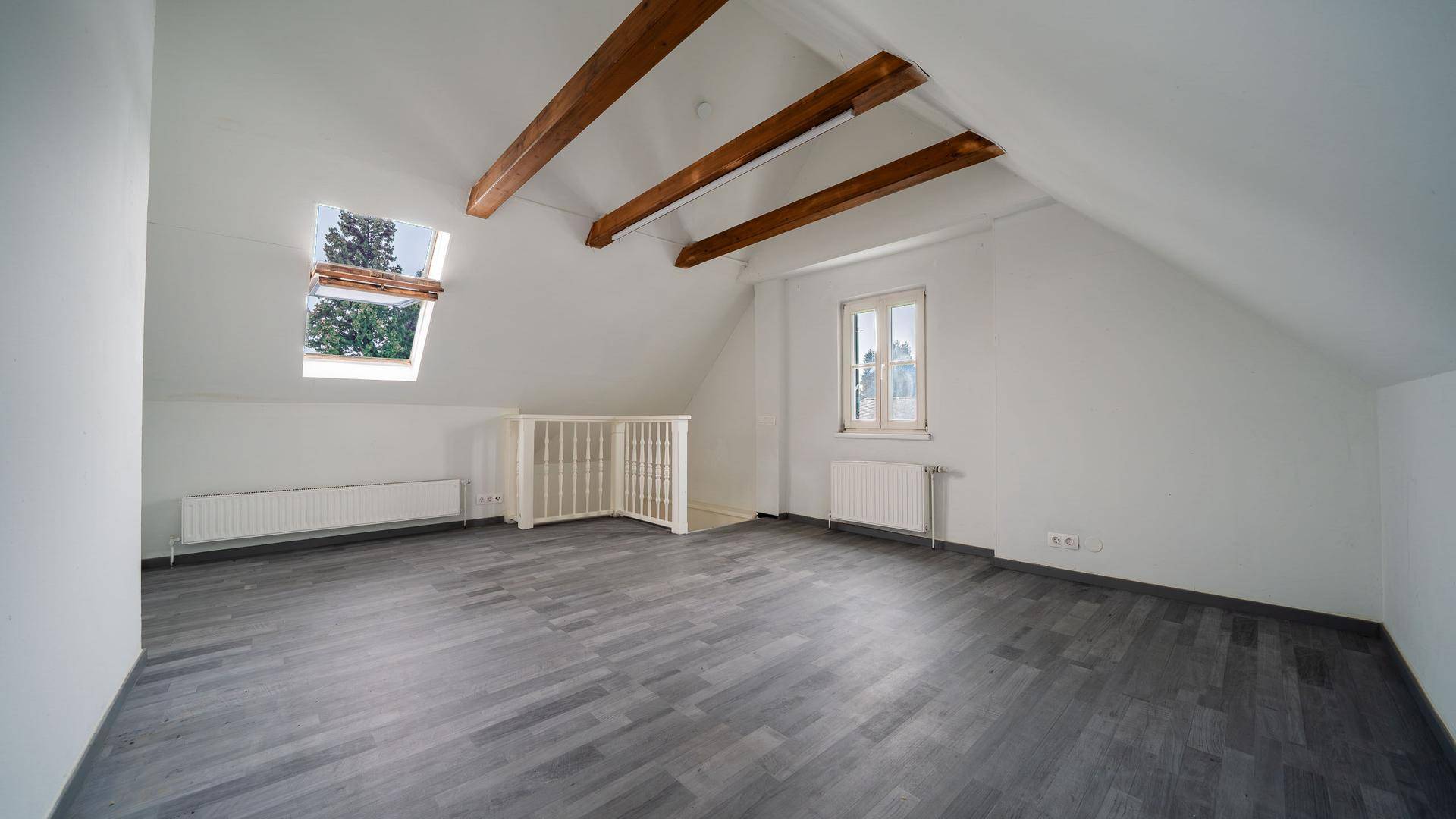 Lichtdurchflutetes Dachzimmer mit sichtbaren Holzbalken, Dachfenster und Laminatboden, sehr geräumig.
