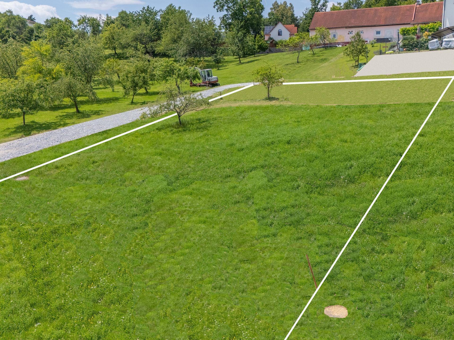Grünes Grundstück mit markierten Grenzen, einem Feldweg und traditionellen Häusern im Hintergrund.