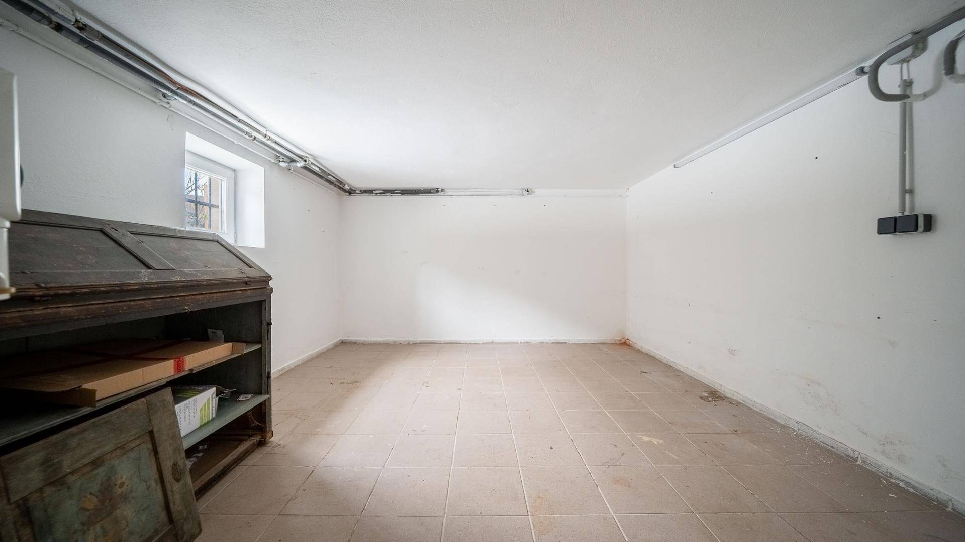Heller Kellerraum mit Fliesenboden, sichtbaren Leitungen und kleinem Fenster, ideal für Lagerung.