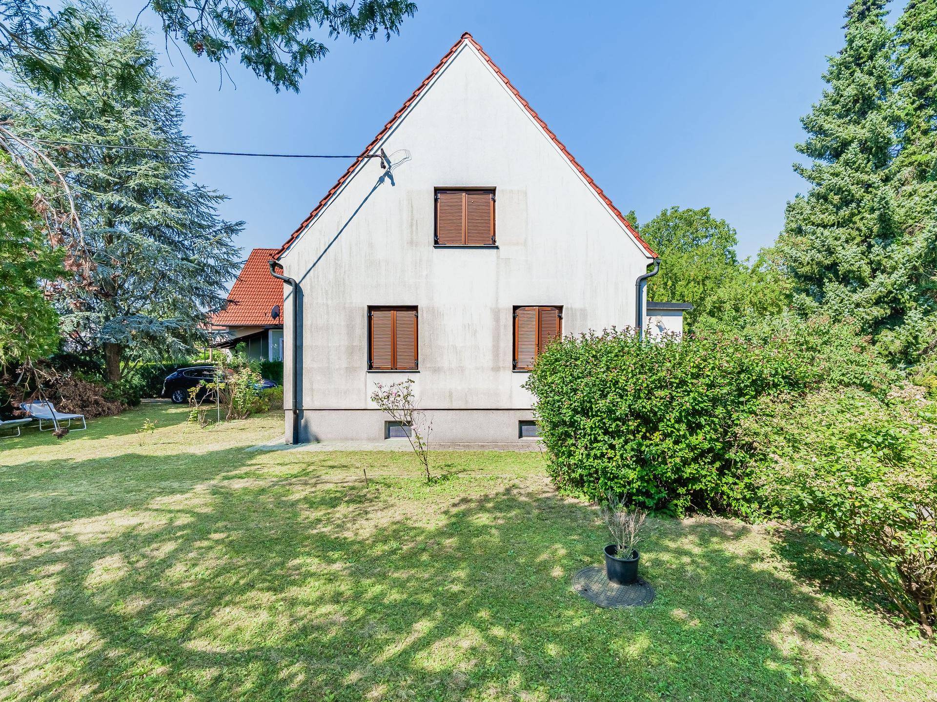 Rückseite des Hauses mit weißer Fassade, braunen Fensterläden und weitläufigem Garten.