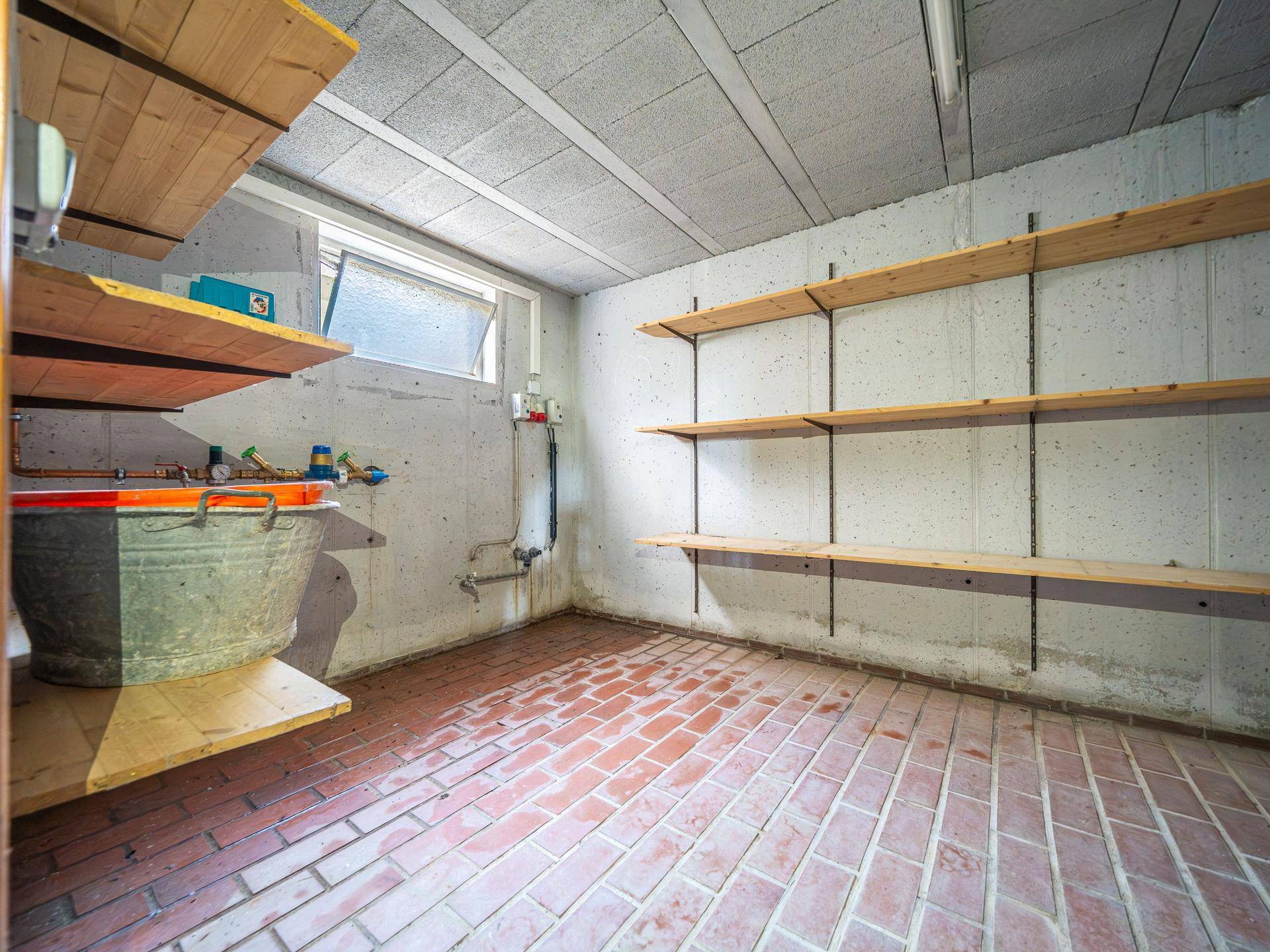 Kellerraum mit Waschbecken, Regalen und Ziegelfliesenboden, ideal als Hauswirtschaftsraum.