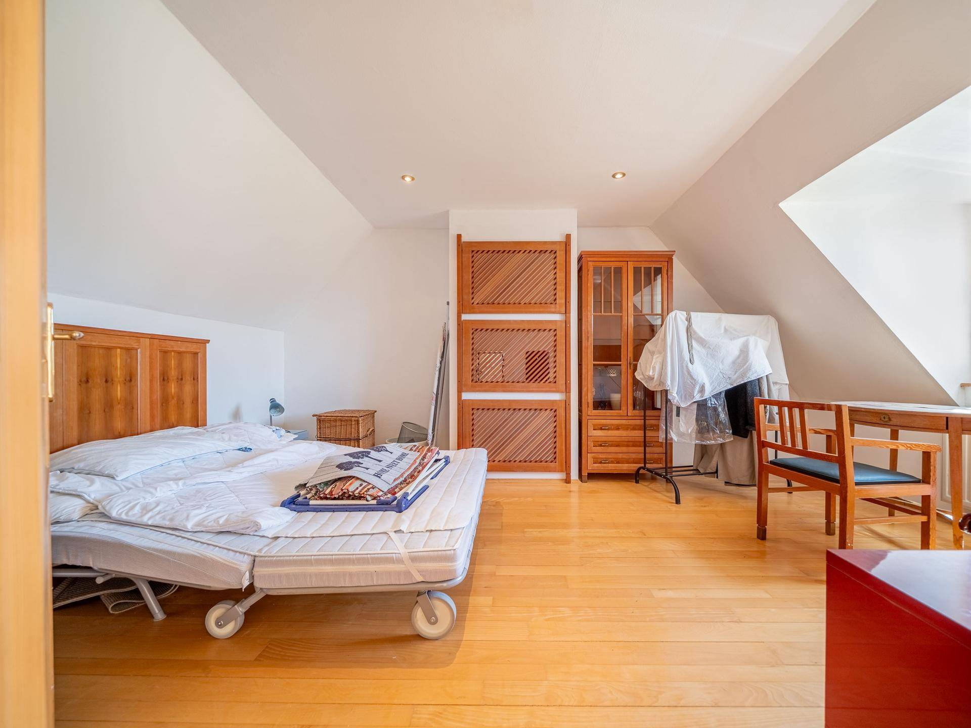 Helles Dachgeschoss-Schlafzimmer mit Holzfußboden, Bett und Stauraum unter der Schräge.