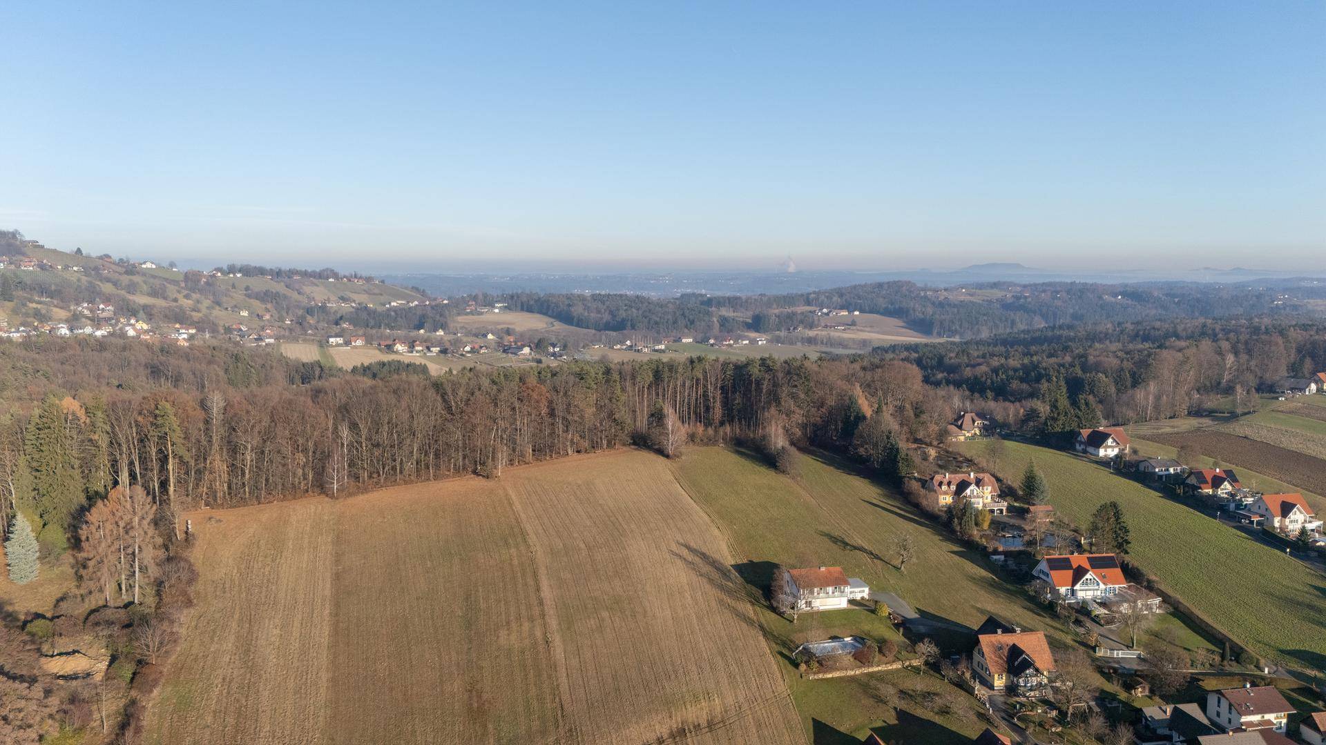 Weitläufige Landschaft mit großen Waldflächen, Feldern und verstreuten Häusern an den Hängen in der Ferne.