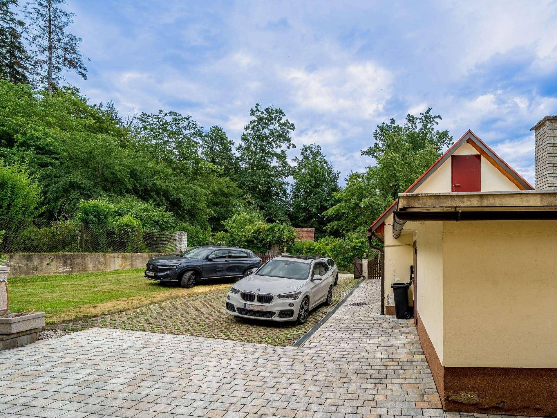 Einfahrt mit zwei Autos und gepflastertem Bereich neben dem Haus und Grünfläche.