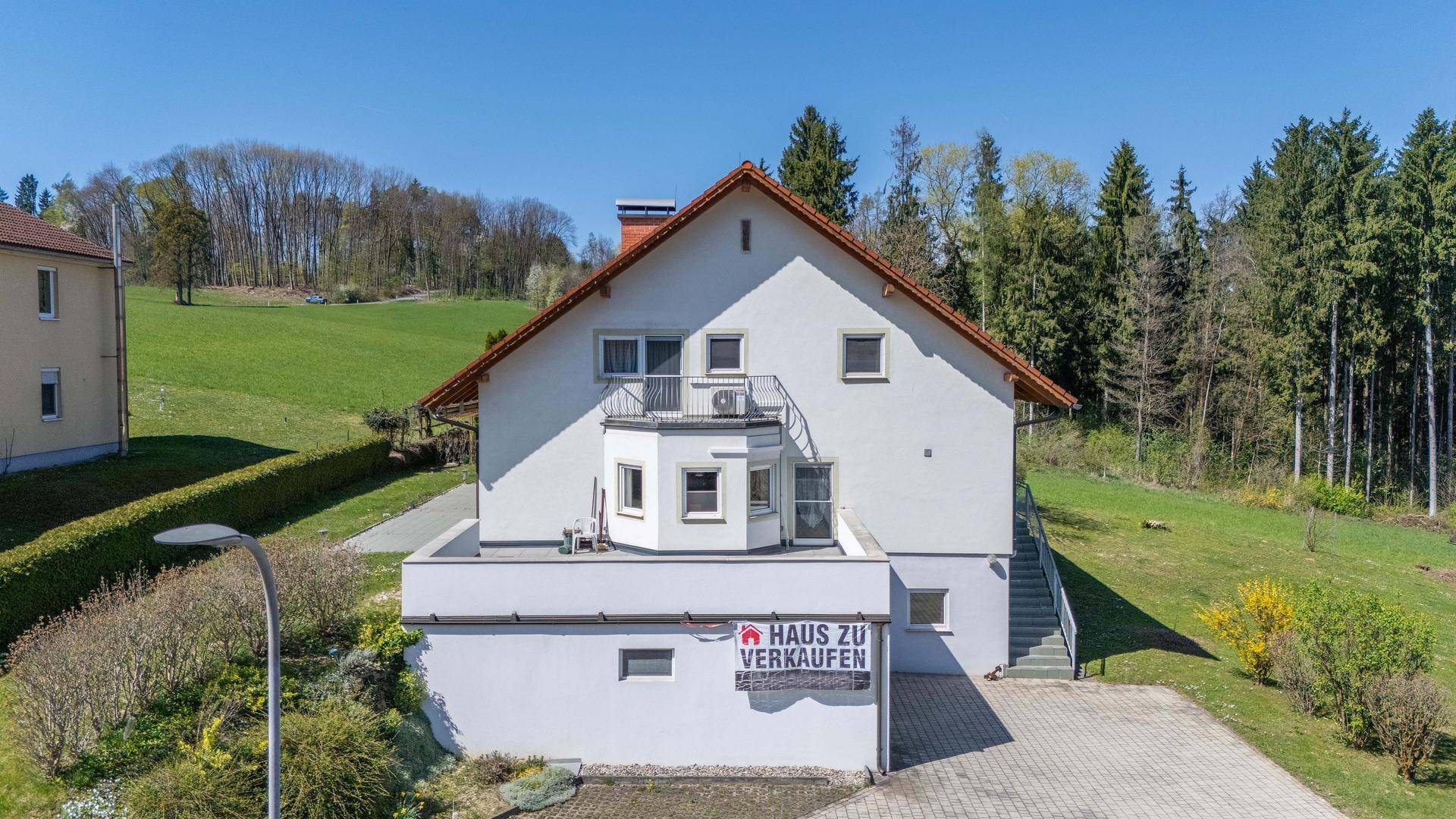 Vorderansicht des Einfamilienhauses mit "Haus zu verkaufen"-Schild und Garage.