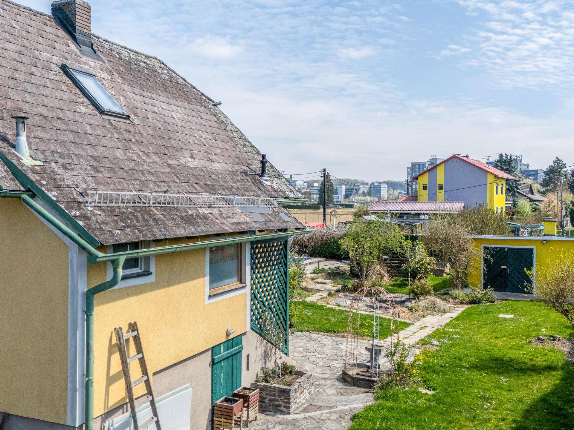 Rückseite des Hauses mit Gartenbereich, Leiter und Blick auf die umliegende Bebauung in der Ferne.