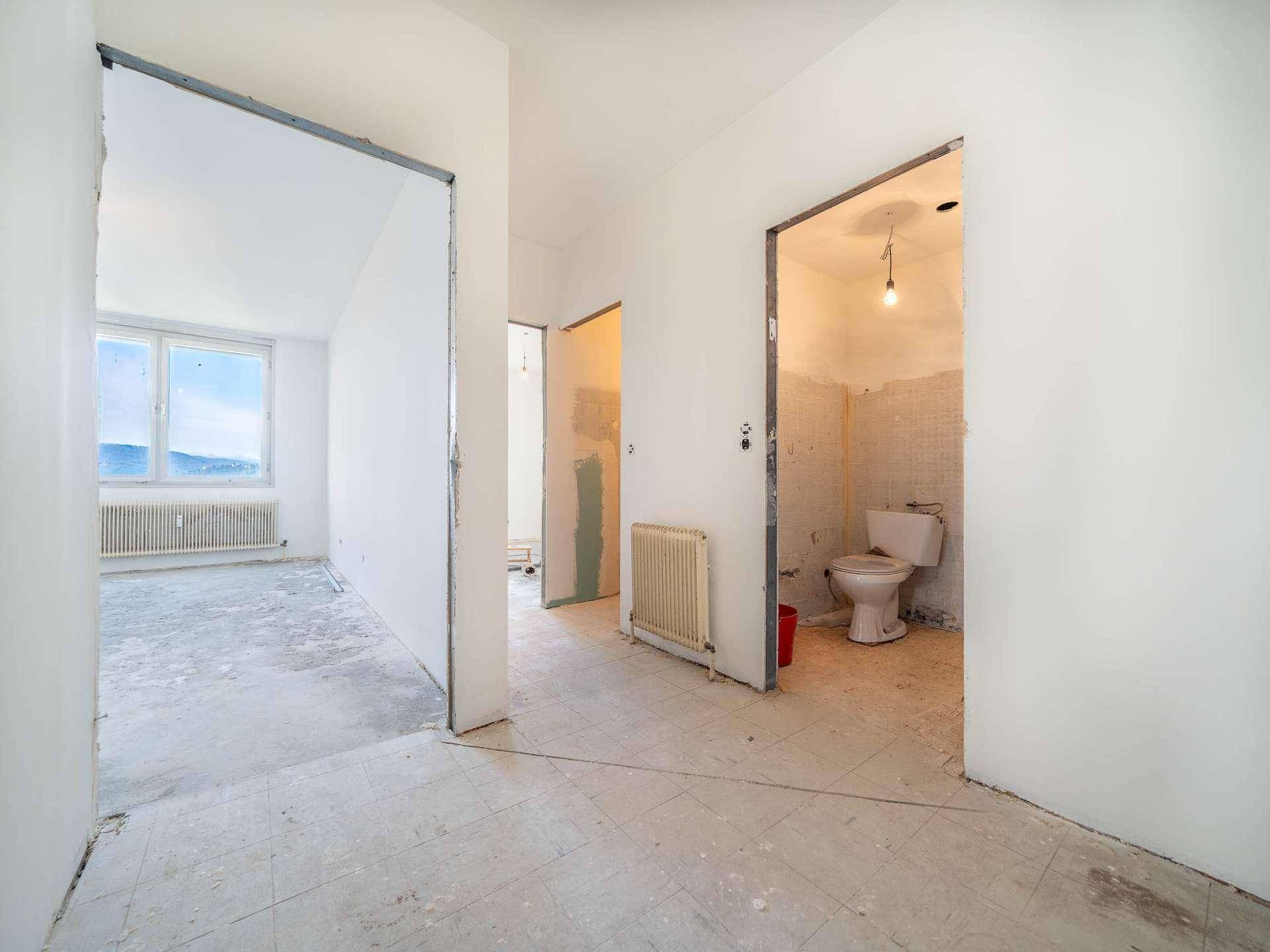 Flur in Renovierung mit Blick in ein Badezimmer mit Toilette und angrenzendes Zimmer.